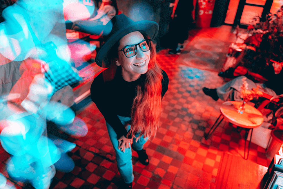 Young hipster woman in glasses and hat dancing in neon lights