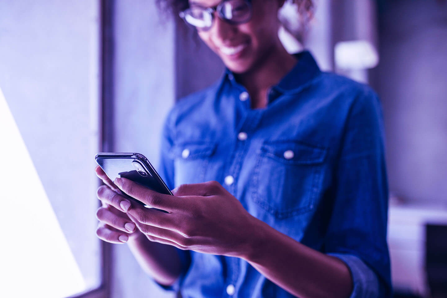 Businesswoman standing in office and using her mobile phone. Focus on smart phone in hand of a female wearing casuals.