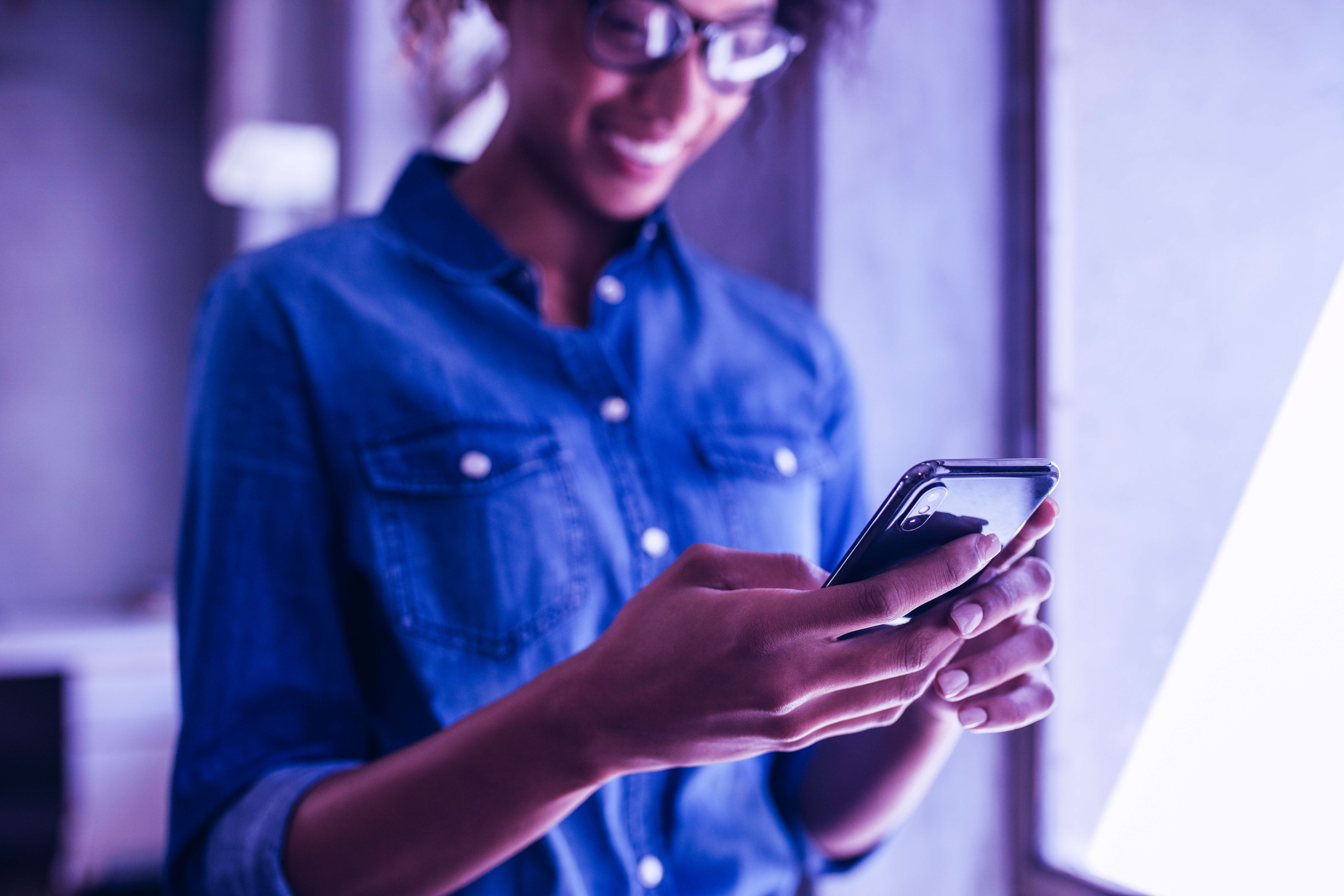 Businesswoman standing in office and using her mobile phone. Focus on smart phone in hand of a female wearing casuals.