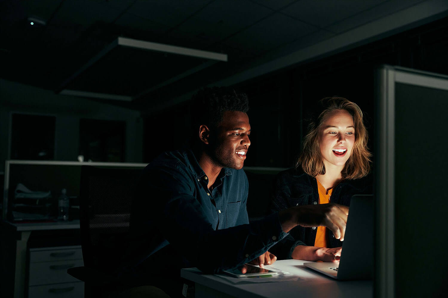 Happy businessman and businesswoman working on laptop overtime in night time