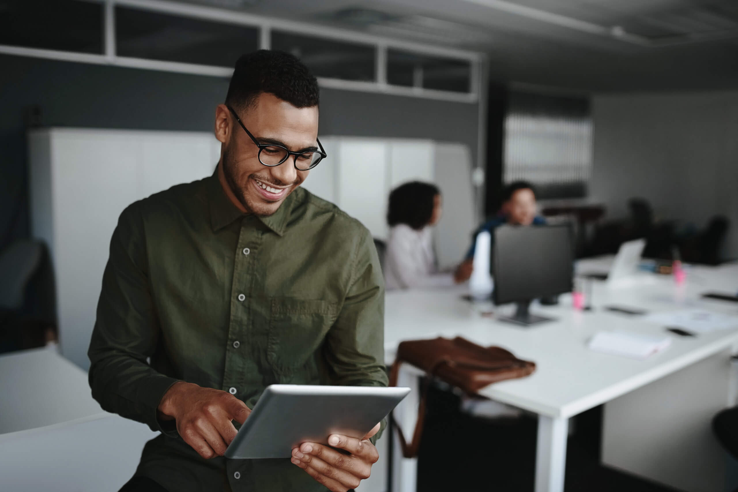 Cheerful young businessman using digital tablet smiling while his colleagues working at the background