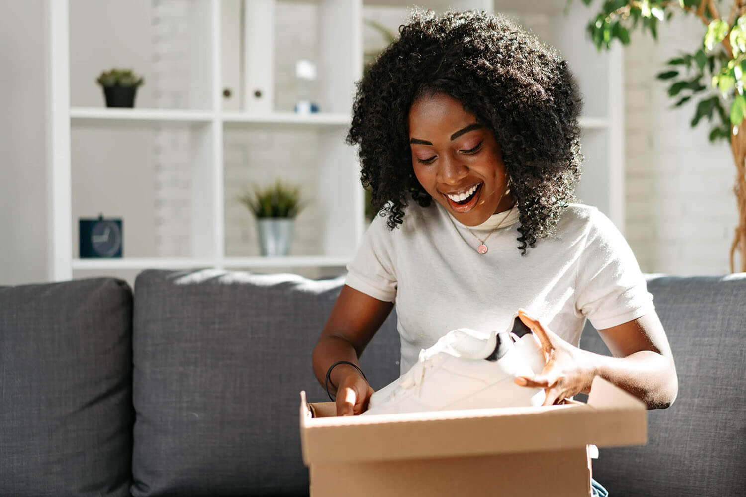 Young african woman sit on couch at home unpacking parcel cardboard box with online purchase