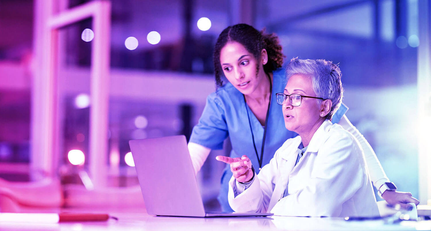 two women in scrubs talking and looking at computer