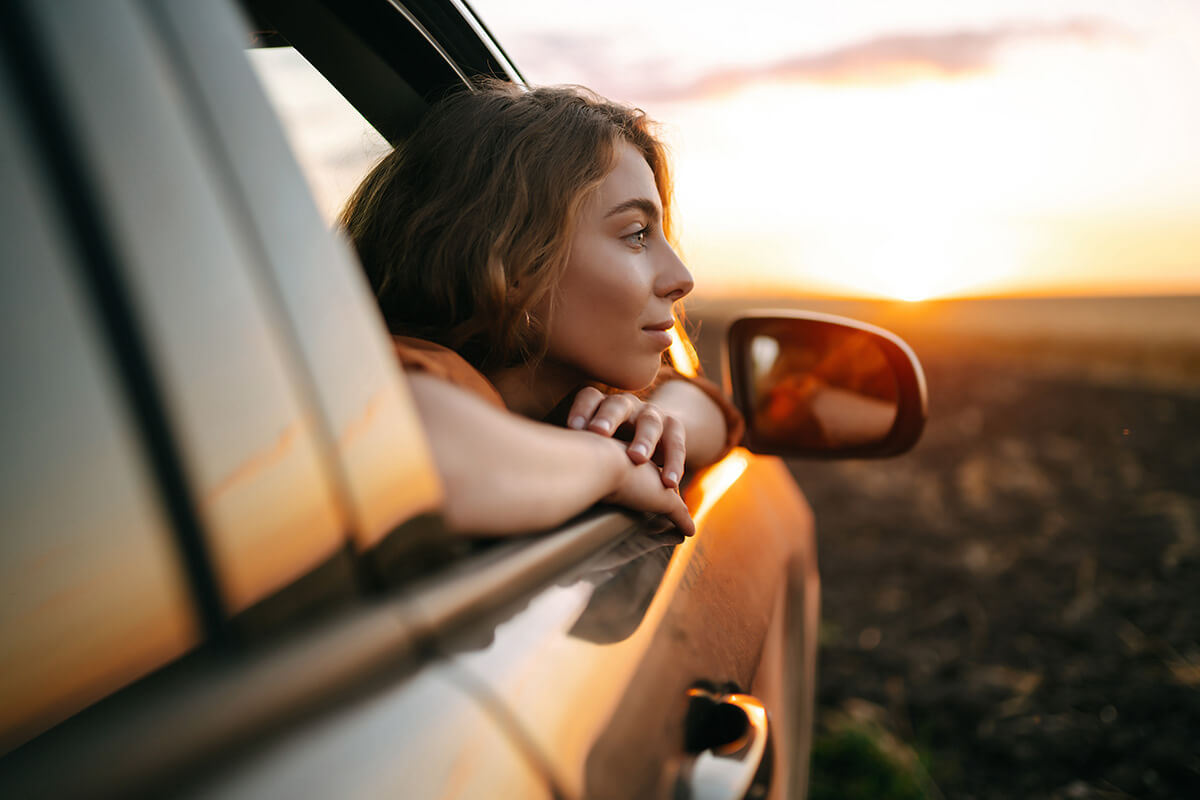 Woman watching sunset from passenger side of vehicle