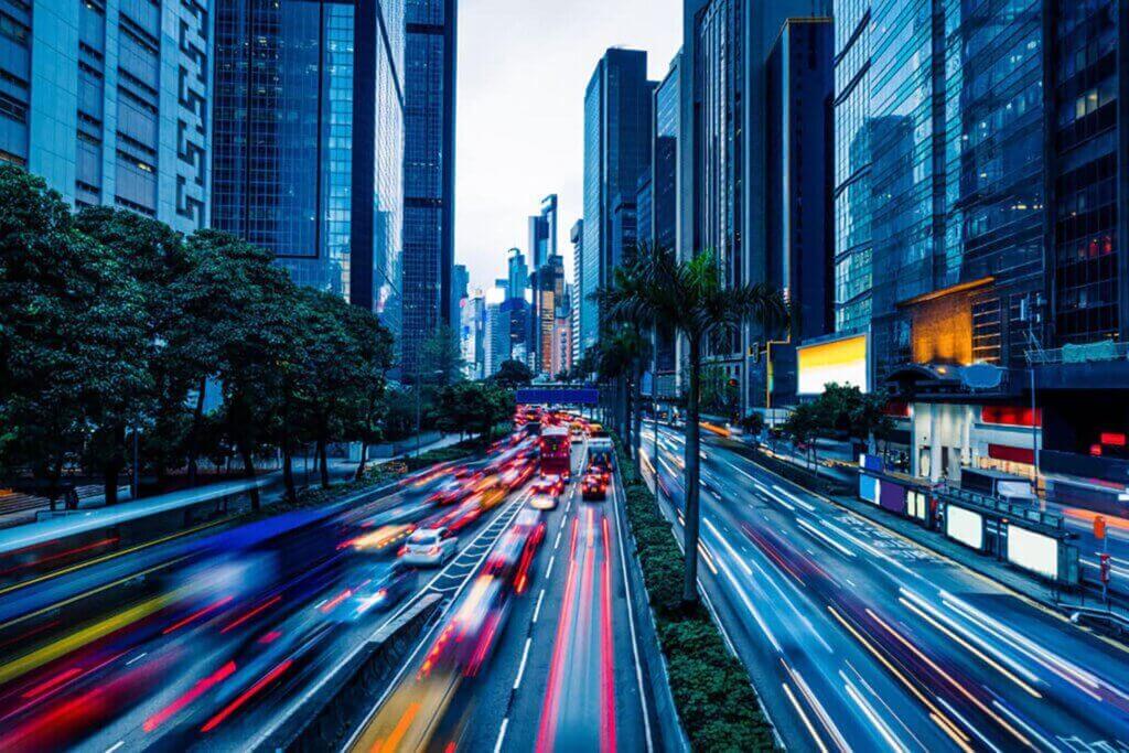 Twilight cityscape with long exposure light trails from moving vehicles on a busy street, flanked by towering skyscrapers