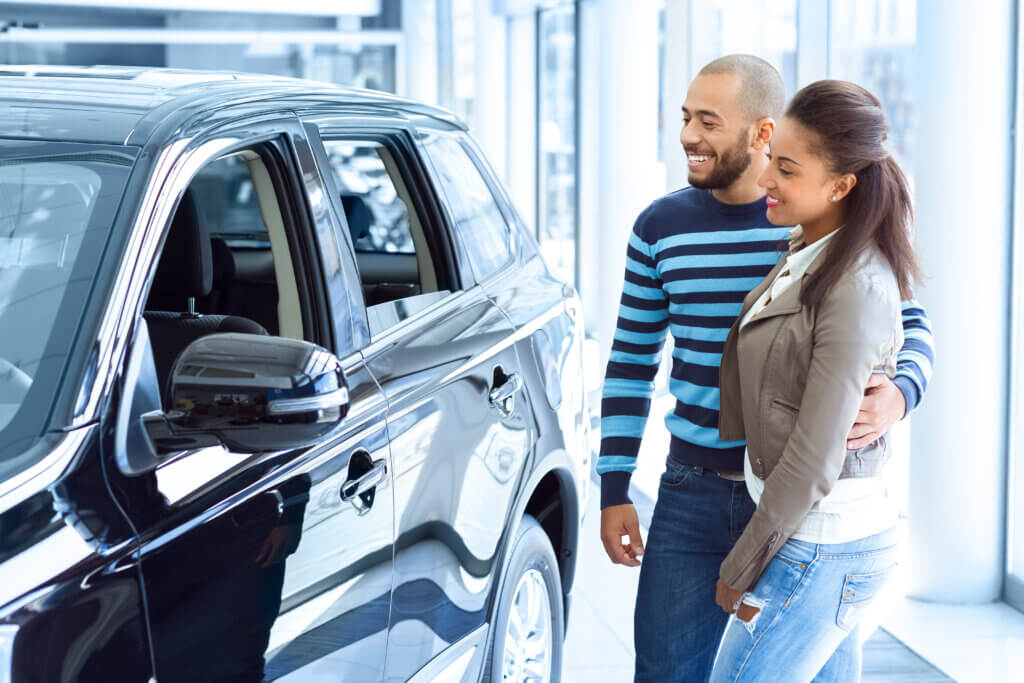 A man and woman car shopper stand beside a new car in a showroom