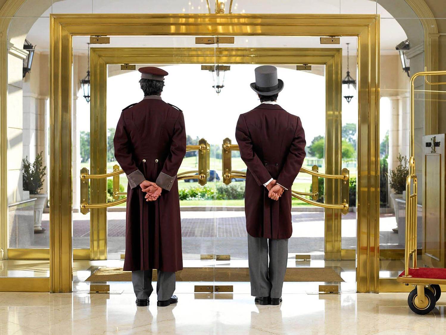 two bellmen standing at the entrance of a classy hotel