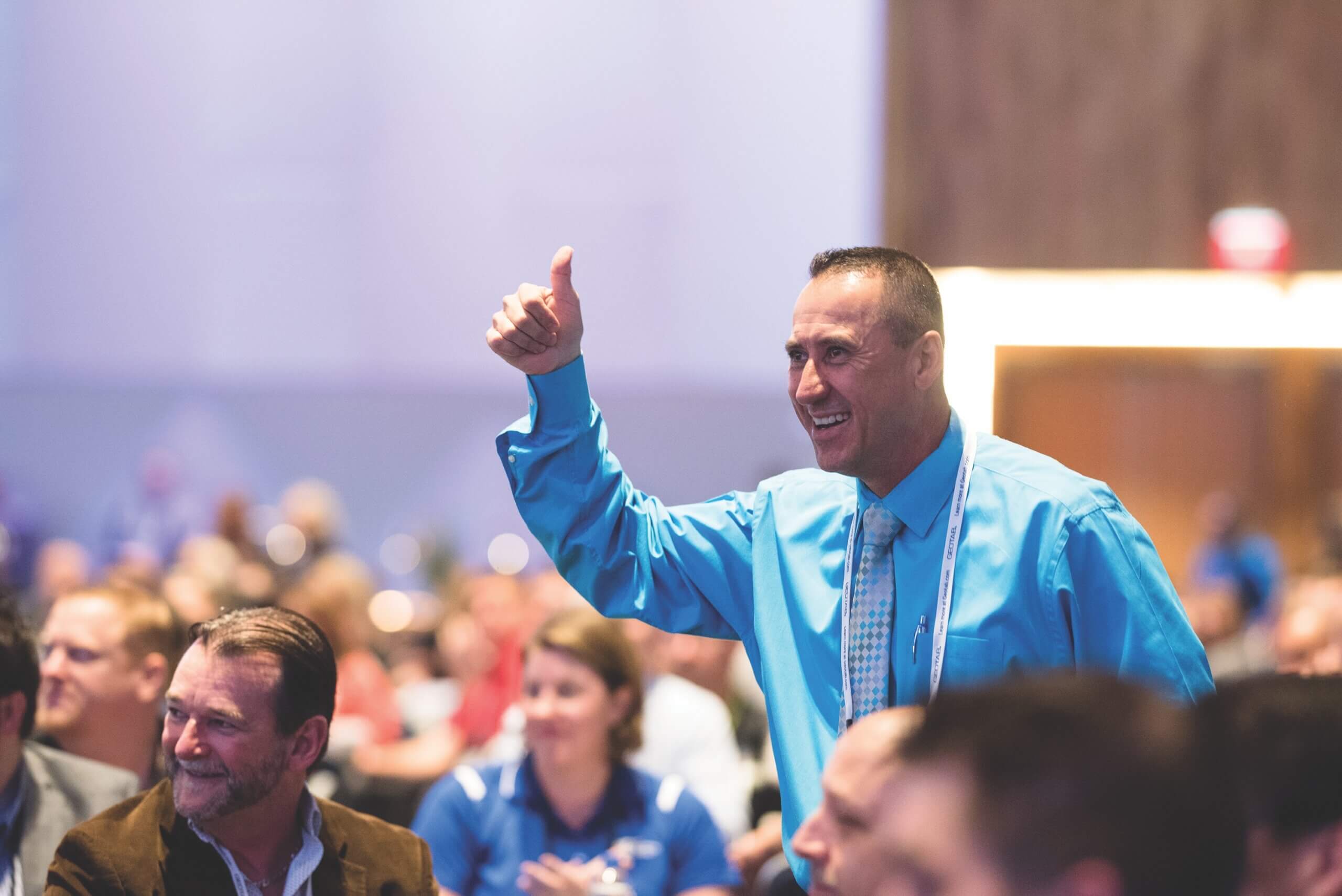 man at conference standing giving thumbs up