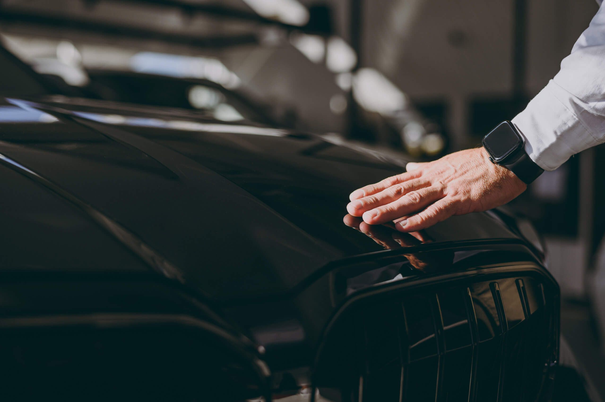 Car buyer's hand on sleek car hood in showroom.